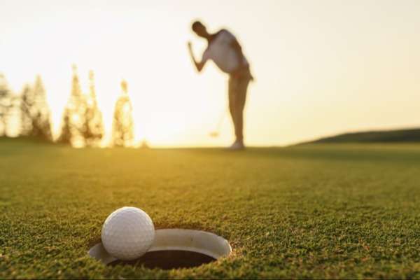 Un giocatore di golf, in controluce, guarda la pallina entrare in buca.