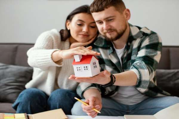 Coppia seduta sul divano che tiene in mano un modellino di casa mentre pianifica l’acquisto dell’abitazione
