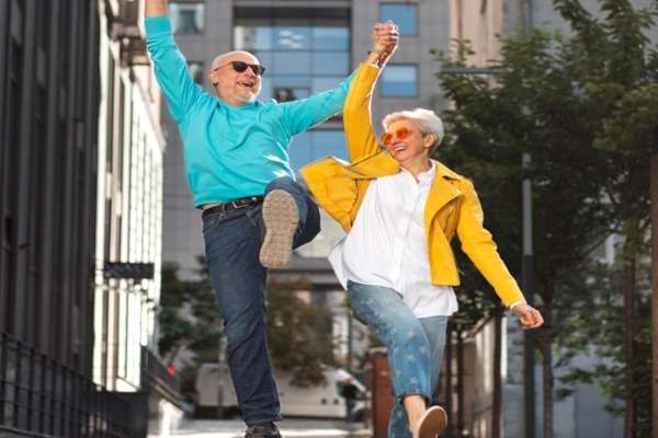 Due adulti anziani che saltano mano nella mano in una strada di città, sorridenti e pieni di energia
