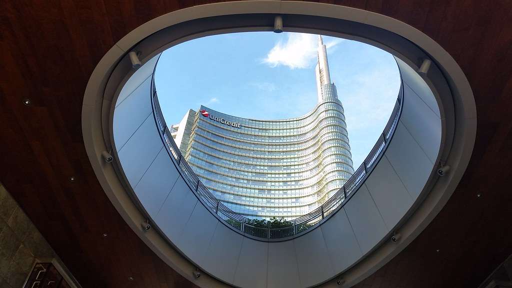 Grattacielo Unicredit a Milano fotografato dal basso attraverso un'apertura ovale, con la guglia visibile contro il cielo