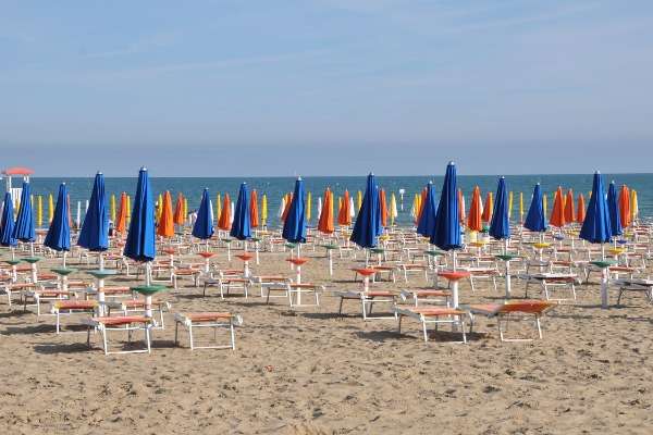 Stabilimento balneare italiano con file di ombrelloni blu, arancioni e gialli e sdraio sulla sabbia