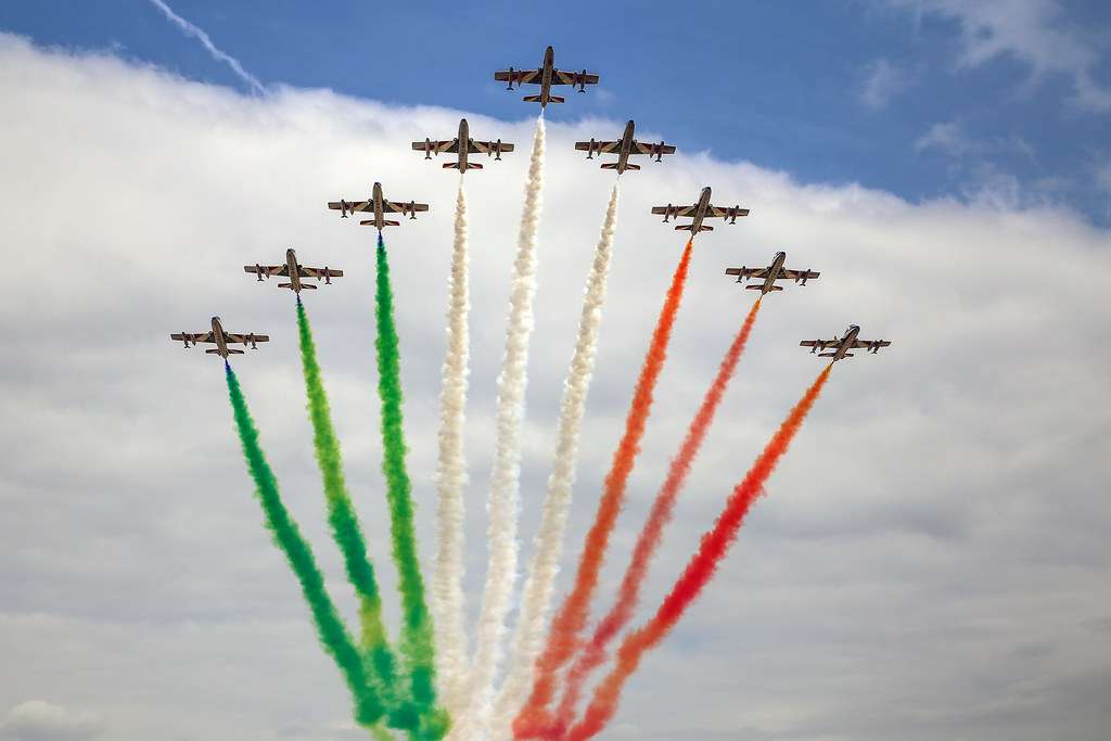 Nove aerei acrobatici delle Frecce Tricolori in formazione a freccia, con scie di fumo verde, bianco e rosso che disegnano la bandiera italiana nel cielo