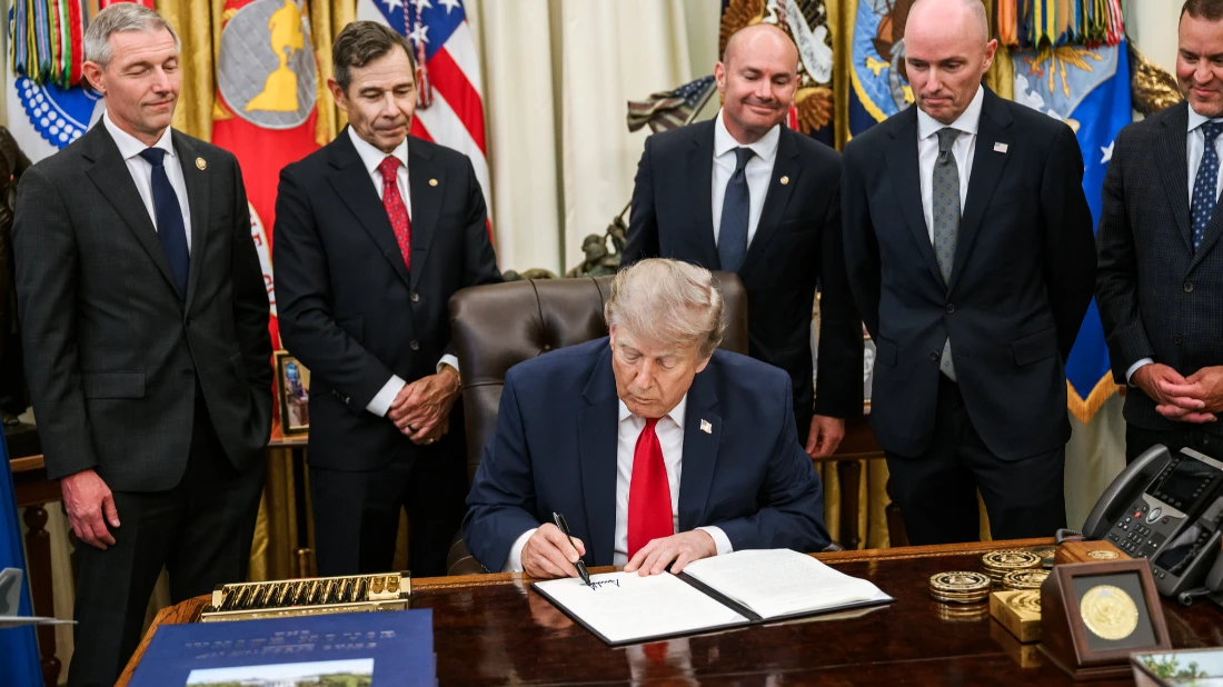 Donald Trump firma un documento nello Studio Ovale, circondato da funzionari, durante l'annuncio dei nuovi dazi sul lavoro forzato