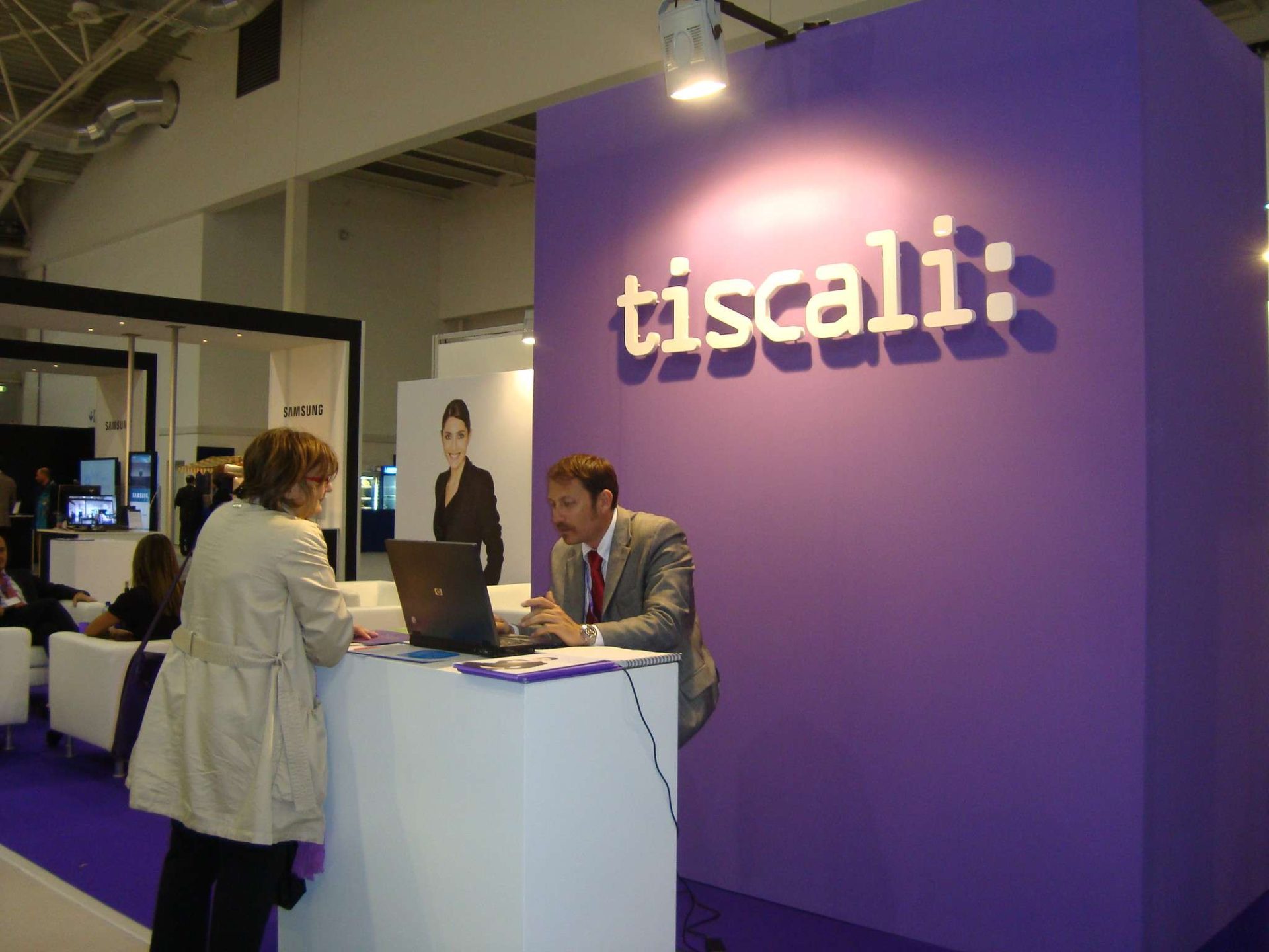 Stand aziendale Tiscali con logo viola durante una fiera del settore tecnologico