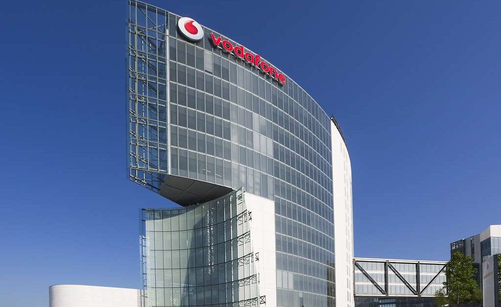 Sede Vodafone con logo aziendale, edificio moderno in vetro contro cielo blu