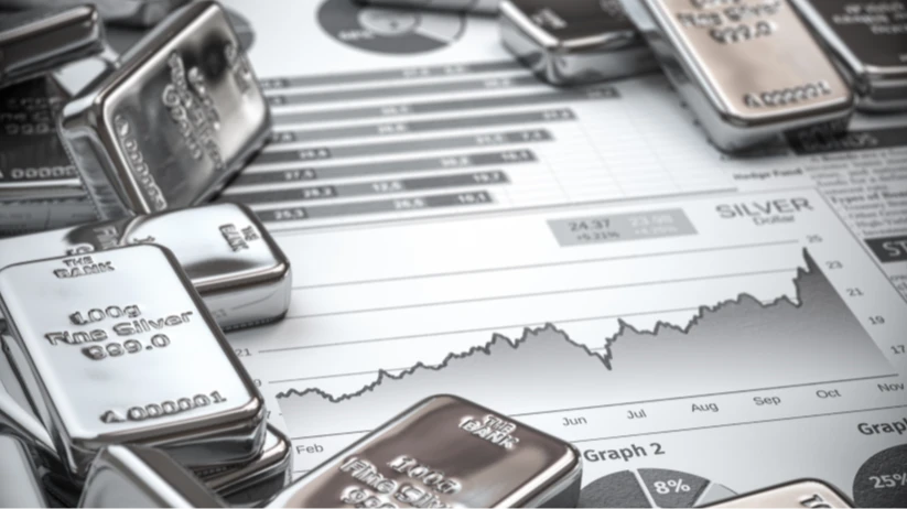 Su un tavolo, poggiati sopra dei grafici finanziari, ci sono dei lingotti d'argento