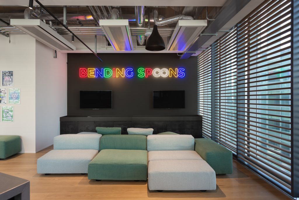 Interno degli uffici di Bending Spoons con insegna luminosa e area relax