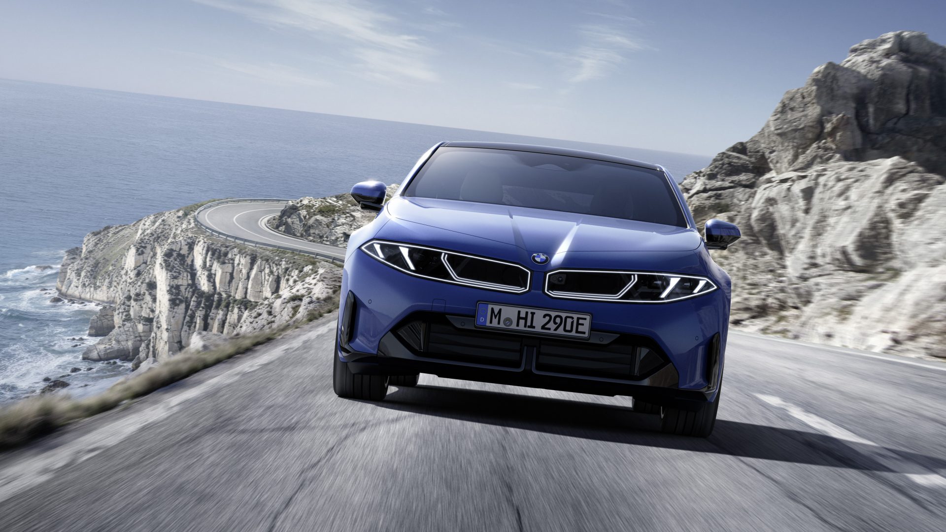 BMW i5 blu su strada panoramica costiera con scogliera e mare sullo sfondo