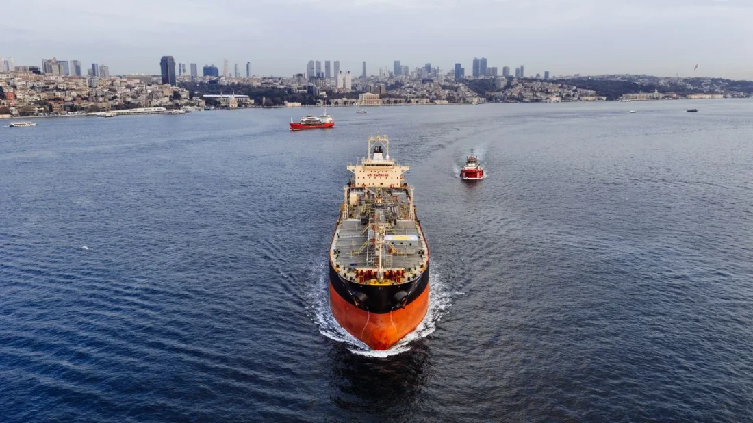 Petroliera scortata da un rimorchiatore attraversa un braccio di mare urbano, con grattacieli e edifici della città sullo sfondo